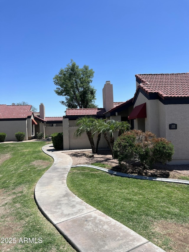 view of front of house featuring a tile roof, stucco siding, a front yard, and a chimney