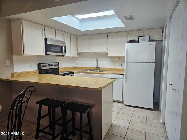 kitchen with appliances with stainless steel finishes, a sink, light countertops, a peninsula, and light tile patterned flooring