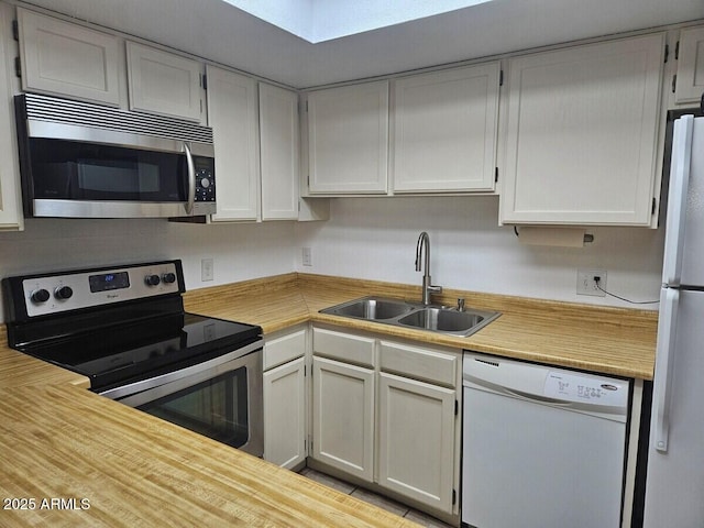 kitchen with appliances with stainless steel finishes, a sink, light countertops, and a skylight