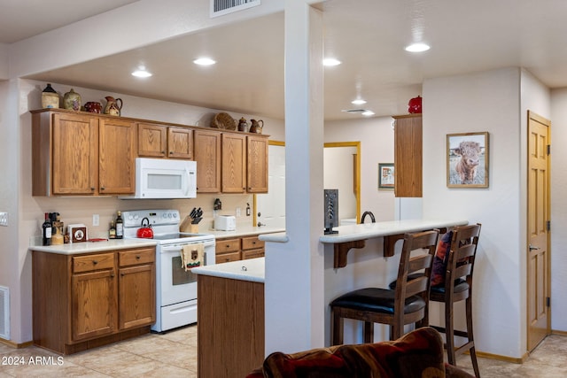 kitchen featuring white appliances, light tile patterned floors, kitchen peninsula, and a breakfast bar