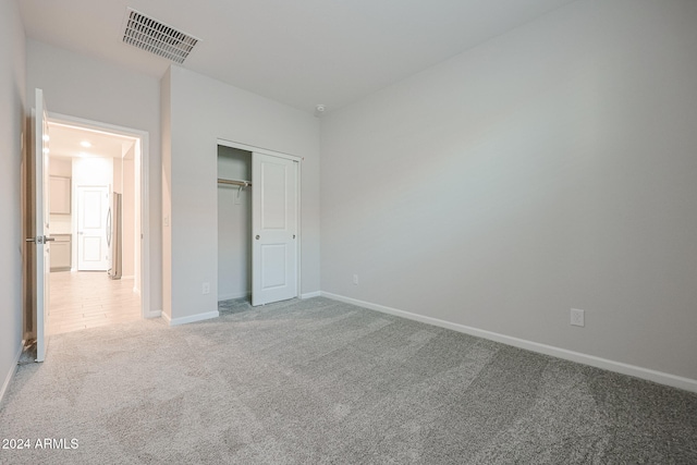 unfurnished bedroom featuring a closet, carpet floors, and stainless steel refrigerator