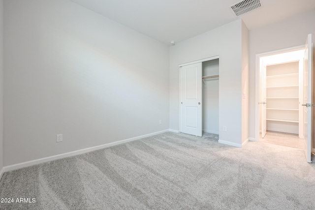 unfurnished bedroom with a closet, a walk in closet, and light colored carpet