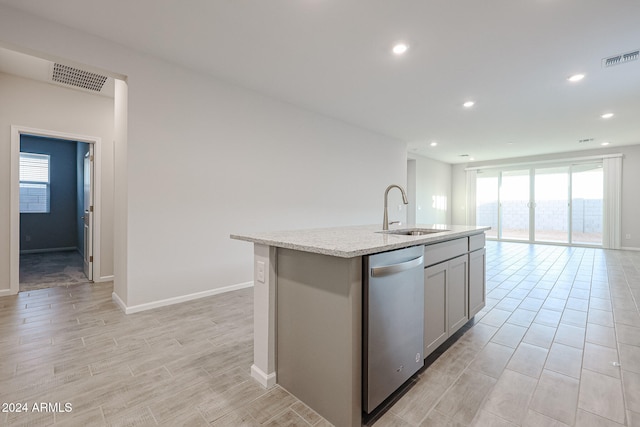 kitchen with a center island with sink, sink, gray cabinets, stainless steel dishwasher, and light stone counters