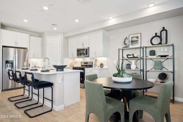 kitchen with appliances with stainless steel finishes, light hardwood / wood-style floors, white cabinetry, and an island with sink