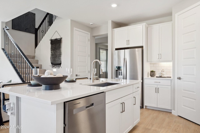 kitchen with appliances with stainless steel finishes, sink, a center island with sink, light hardwood / wood-style flooring, and white cabinets