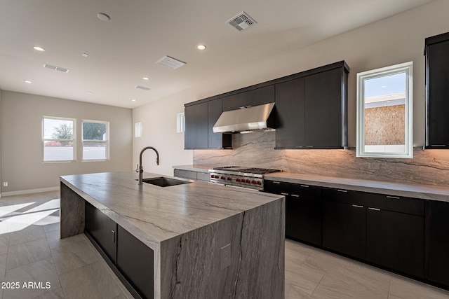 kitchen with sink, high end stove, an island with sink, and range hood