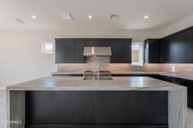 kitchen with decorative backsplash, a kitchen island with sink, and sink