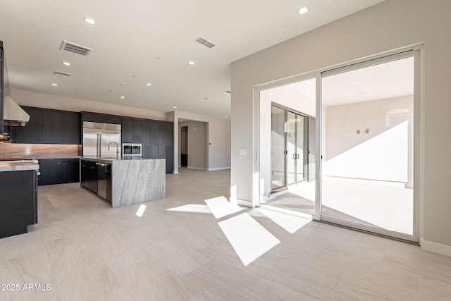 kitchen featuring built in appliances, a kitchen island with sink, and wall chimney exhaust hood