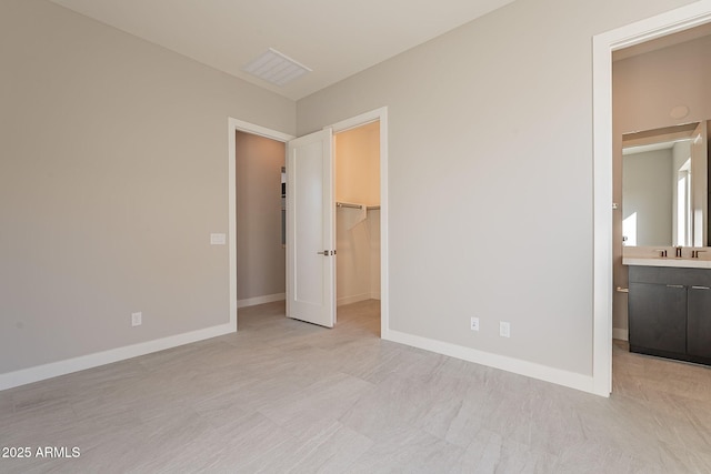 unfurnished bedroom with a closet, a spacious closet, ensuite bath, and sink