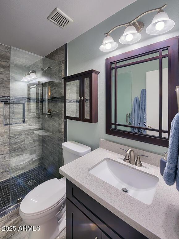 bathroom featuring a tile shower, vanity, and toilet