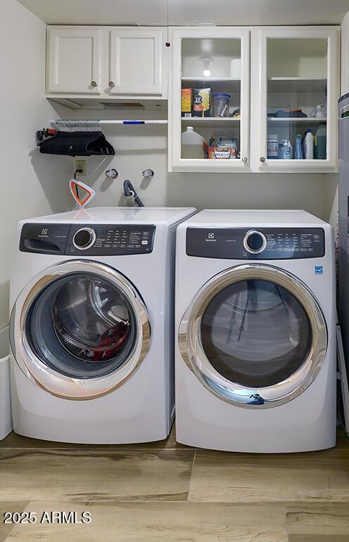 washroom featuring separate washer and dryer, cabinets, and light wood-type flooring