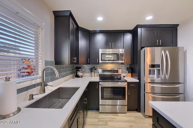 kitchen with sink, light wood-type flooring, appliances with stainless steel finishes, tasteful backsplash, and light stone counters