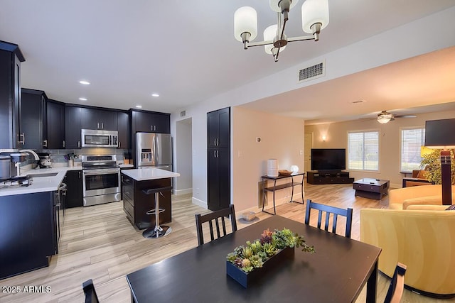 dining space featuring ceiling fan with notable chandelier, light wood-type flooring, and sink