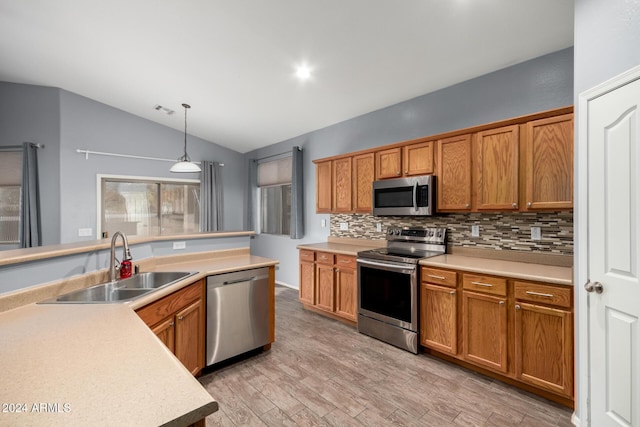 kitchen featuring backsplash, vaulted ceiling, pendant lighting, sink, and appliances with stainless steel finishes