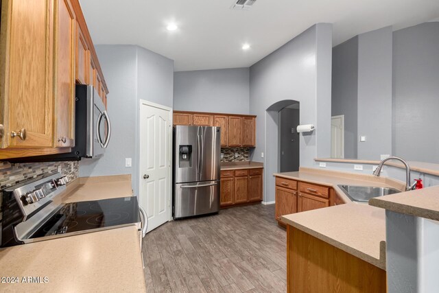 kitchen with stainless steel appliances, decorative backsplash, a high ceiling, light hardwood / wood-style flooring, and sink