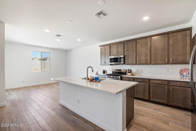 kitchen featuring light hardwood / wood-style flooring, dark brown cabinets, sink, an island with sink, and appliances with stainless steel finishes