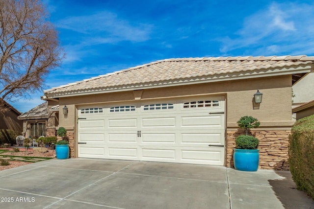 exterior space featuring a garage, driveway, stone siding, and stucco siding