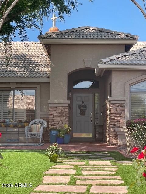 view of exterior entry with stone siding, a lawn, a tile roof, and stucco siding