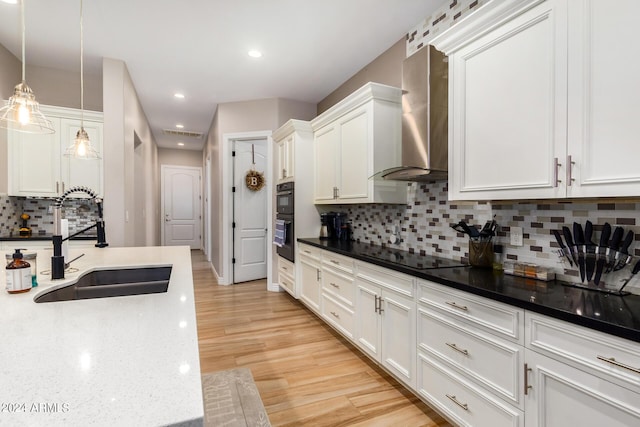 kitchen with wall chimney range hood, sink, hanging light fixtures, black appliances, and white cabinets