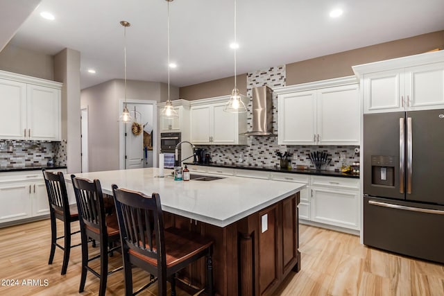 kitchen featuring sink, hanging light fixtures, black appliances, a center island with sink, and wall chimney exhaust hood