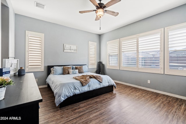 bedroom with ceiling fan, dark wood-type flooring, and a wood stove