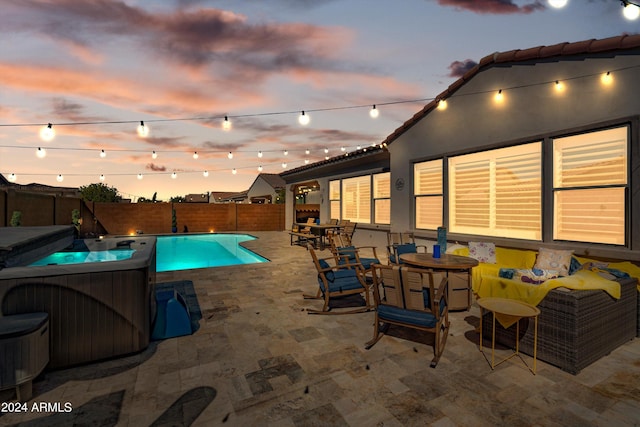 pool at dusk with a hot tub and a patio