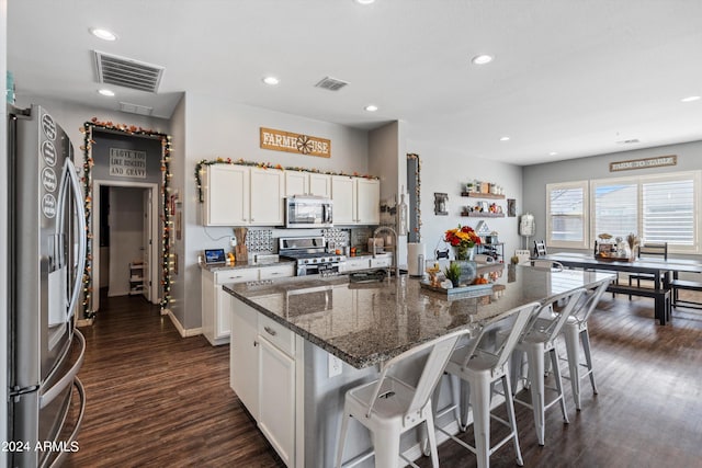 kitchen featuring dark stone counters, dark hardwood / wood-style floors, a kitchen island with sink, white cabinetry, and stainless steel appliances