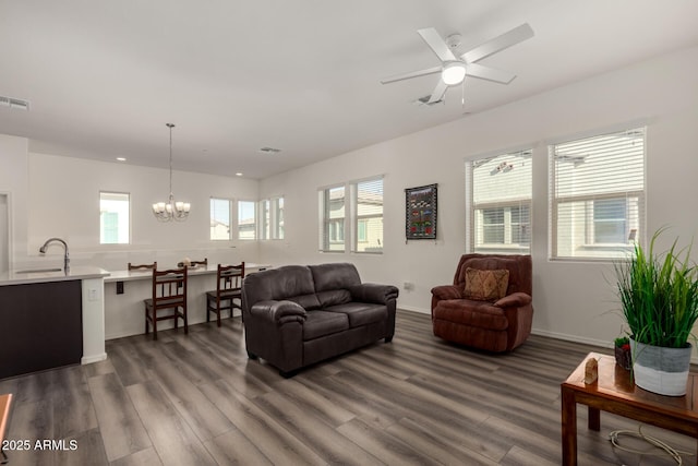 living room featuring dark wood-type flooring, ceiling fan with notable chandelier, and sink