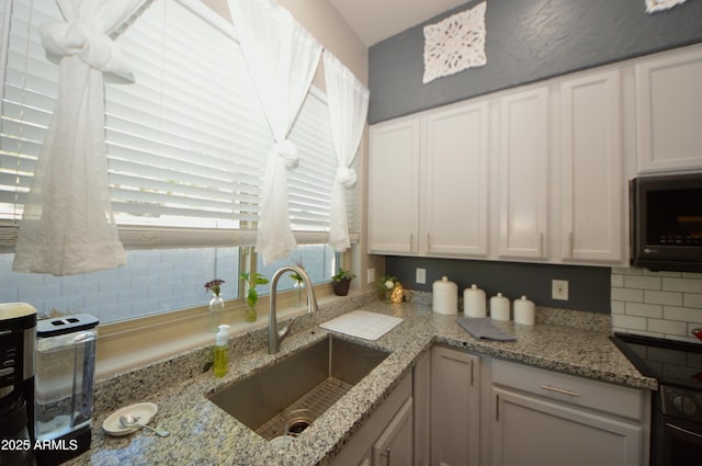 kitchen featuring tasteful backsplash, white cabinetry, light stone counters, and a sink