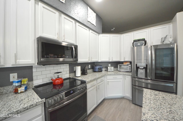 kitchen with appliances with stainless steel finishes, light wood-type flooring, and white cabinets