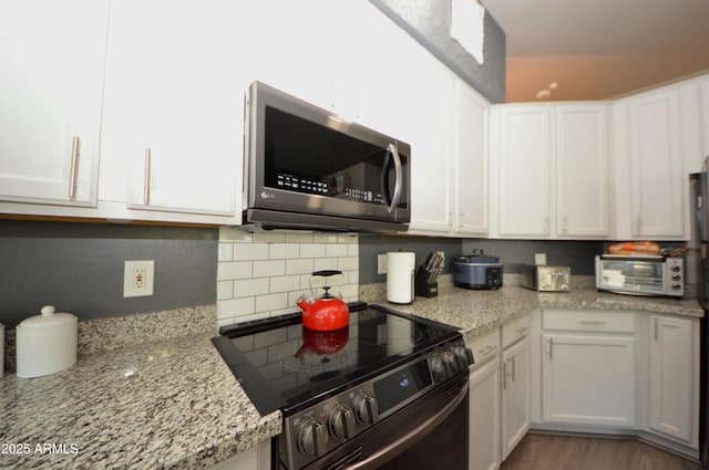 kitchen with white cabinets, electric range oven, light stone counters, stainless steel microwave, and wood finished floors