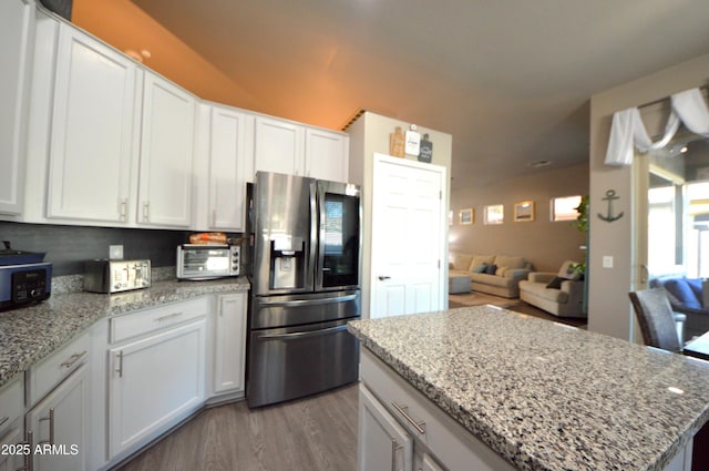 kitchen with light stone counters, a toaster, stainless steel refrigerator with ice dispenser, white cabinets, and wood finished floors