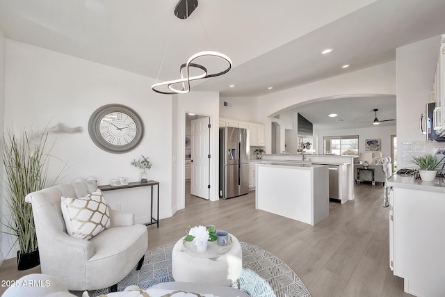 living area featuring arched walkways, recessed lighting, light wood-style flooring, vaulted ceiling, and ceiling fan