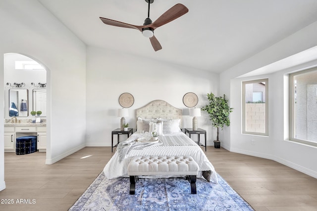 bedroom with arched walkways, light wood-style flooring, ensuite bathroom, vaulted ceiling, and a sink