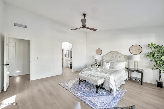 bedroom featuring arched walkways, visible vents, light wood-style flooring, and a high ceiling