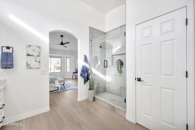 ensuite bathroom with a stall shower, ceiling fan, vanity, wood finished floors, and baseboards