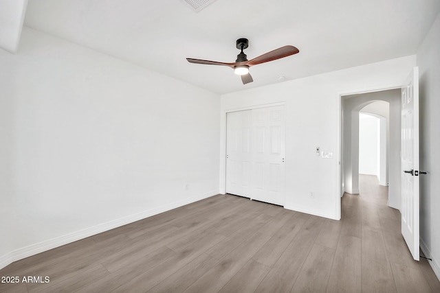 unfurnished bedroom featuring arched walkways, wood finished floors, a ceiling fan, baseboards, and a closet