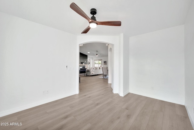 spare room with a ceiling fan, arched walkways, baseboards, and wood finished floors