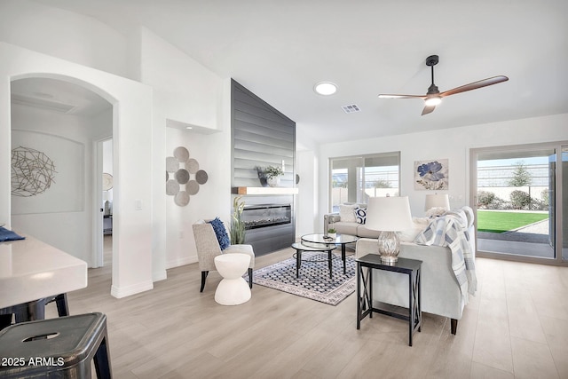 living room with a wealth of natural light, a glass covered fireplace, visible vents, and light wood-style floors