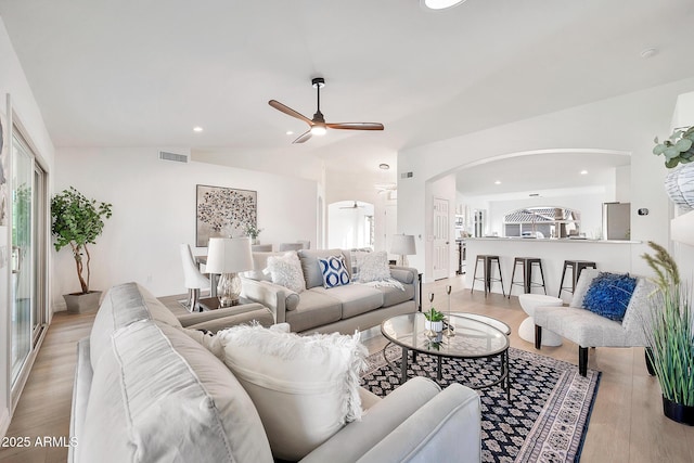 living room with arched walkways, lofted ceiling, visible vents, light wood-style floors, and ceiling fan