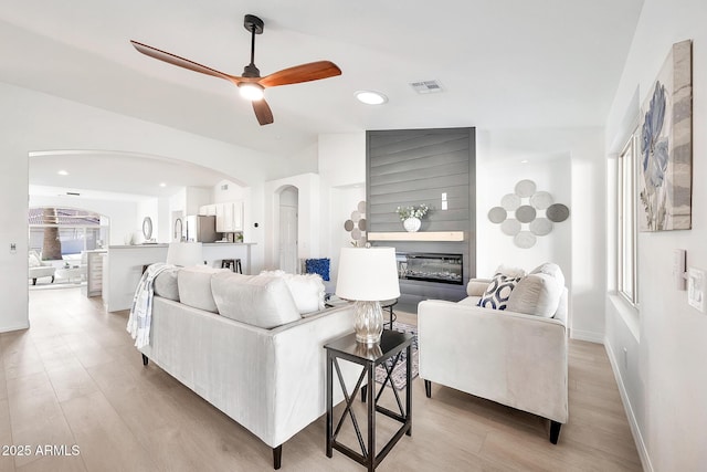 living area featuring lofted ceiling, a large fireplace, light wood-style flooring, and arched walkways