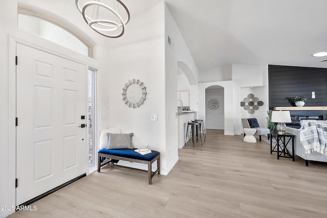 entryway featuring baseboards, arched walkways, a high ceiling, light wood-type flooring, and a notable chandelier