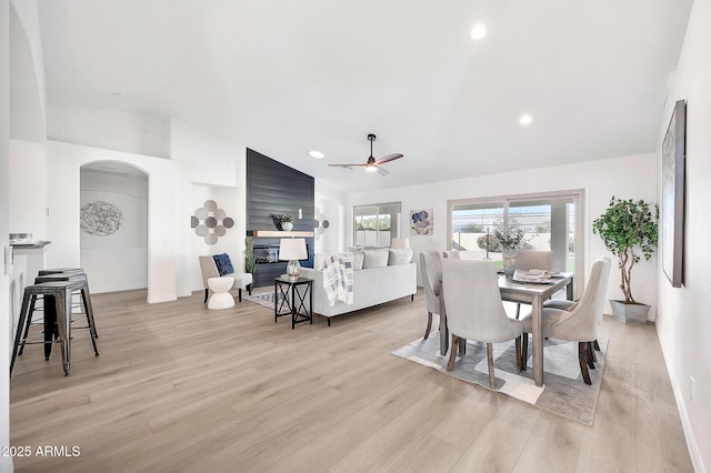 dining room featuring arched walkways, light wood finished floors, recessed lighting, vaulted ceiling, and a multi sided fireplace