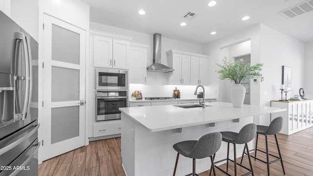 8140 E June St, Mesa, AZ 85207 - kitchen with stainless steel appliances, wall chimney exhaust hood, a kitchen bar, wood finished floors, and white cabinets