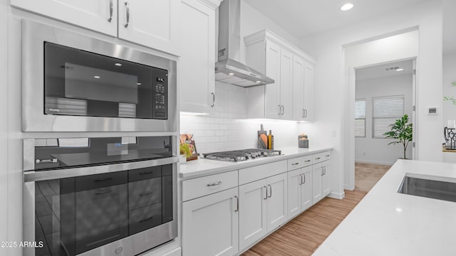 8140 E June St, Mesa, AZ 85207 - kitchen with appliances with stainless steel finishes, wall chimney range hood, light countertops, white cabinetry, and light wood-style flooring