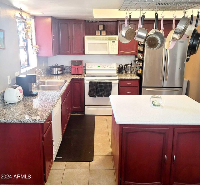 kitchen with dark brown cabinets, a kitchen island, light tile patterned floors, white appliances, and a sink