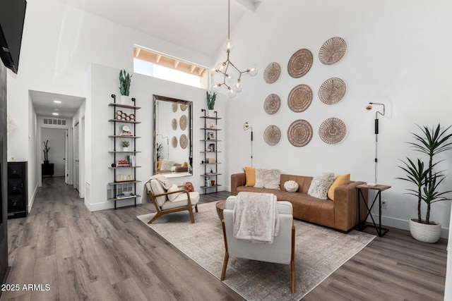 living area with wood finished floors, an inviting chandelier, baseboards, visible vents, and high vaulted ceiling