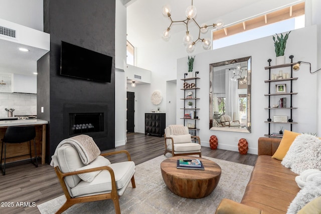 living room with wood finished floors, an inviting chandelier, a fireplace, visible vents, and a high ceiling