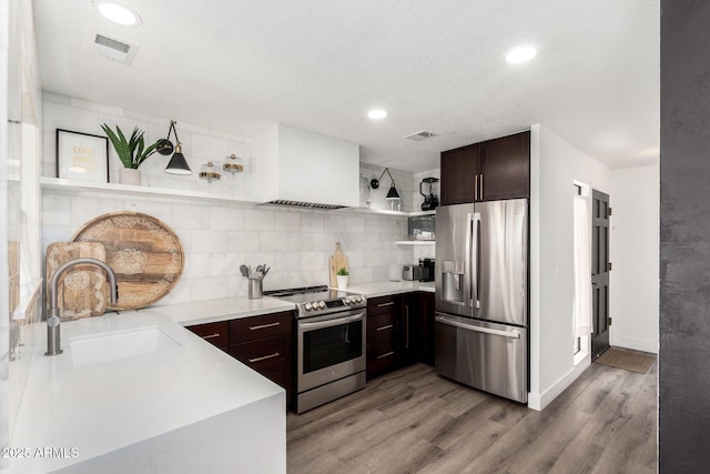 kitchen with a sink, open shelves, dark brown cabinetry, light wood-style flooring, and appliances with stainless steel finishes