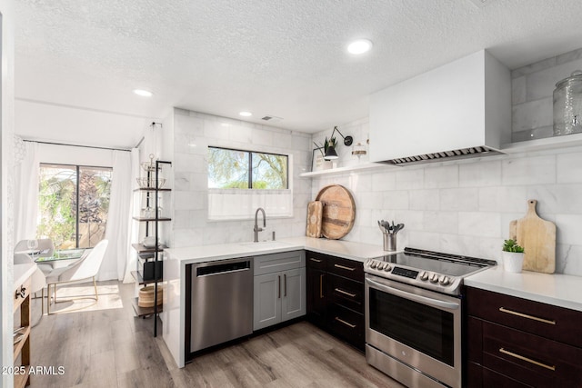 kitchen featuring stainless steel appliances, premium range hood, a textured ceiling, and a sink